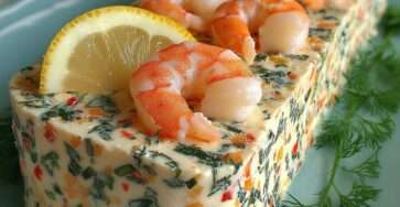 Terrine froide crémeuse aux crevettes et légumes colorés, démoulée et décorée d’aneth et de citron.