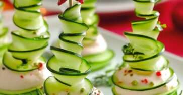 Petits sapins de concombre roulés en spirale sur base de fromage frais aux herbes, décorés d’étoiles rouges.