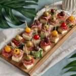 Mini brochettes apéritives avec cubes de fromage, salami plié, olives et tomates cerises présentées sur un plateau.