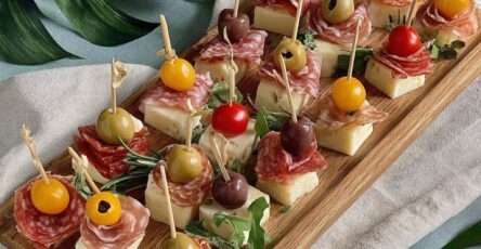Mini brochettes apéritives avec cubes de fromage, salami plié, olives et tomates cerises présentées sur un plateau.