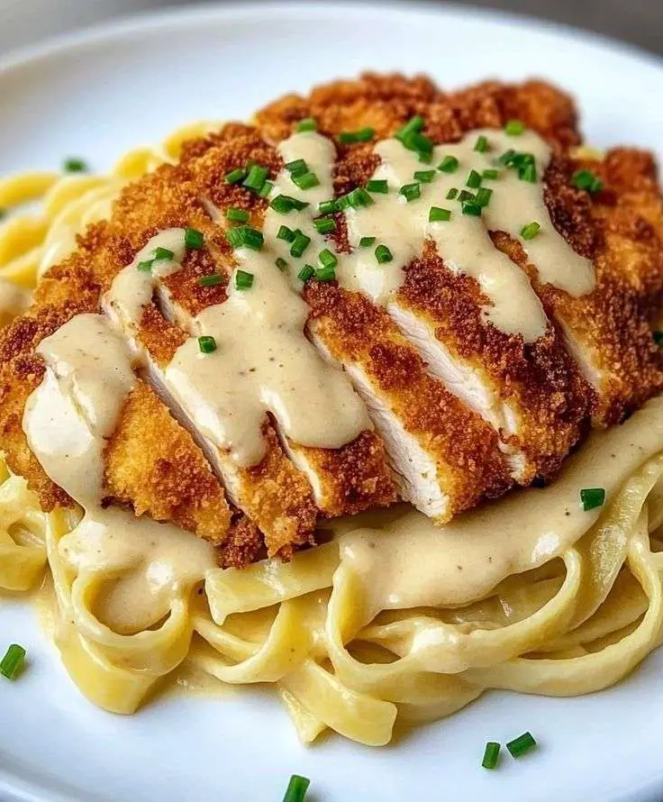 Assiette de fettuccines Alfredo crémeuses garnies de tranches de poulet croustillant doré.