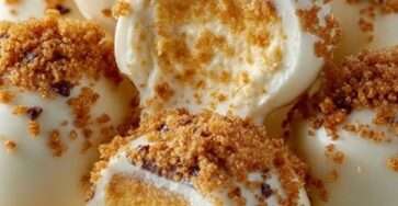 Boules cheesecake à la citrouille enrobées de chocolat blanc, décorées de miettes de biscuits et disposées sur une plaque.