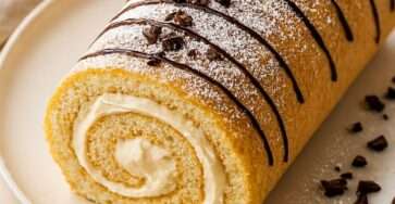 Gâteau roulé à la vanille garni de crème fouettée, saupoudré de sucre glace et décoré de copeaux de chocolat.