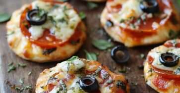 Mini-pizzas apéritives dorées au four, garnies de sauce tomate, mozzarella fondue et tranches de pepperoni avec un peu d’herbes