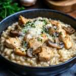 Assiette de risotto crémeux au poulet et aux champignons, parsemée de parmesan et de persil frais