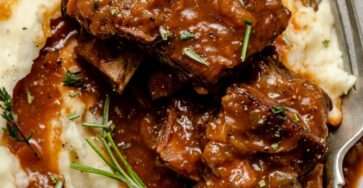 Côtes de bœuf braisées au vin rouge, fondantes et nappées de sauce, servies avec une purée de pommes de terre crémeuse et des herbes fraîches