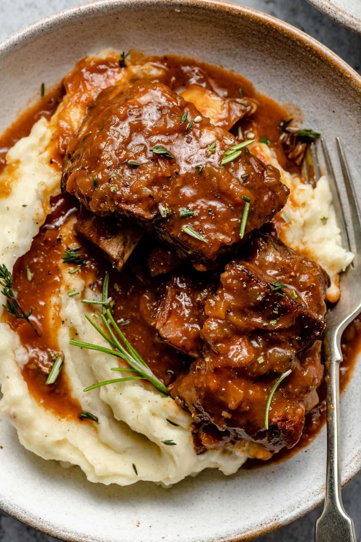 Côtes de bœuf braisées au vin rouge, fondantes et nappées de sauce, servies avec une purée de pommes de terre crémeuse et des herbes fraîches