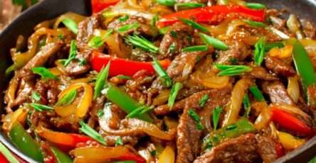 Wok de bœuf sauté aux poivrons rouges et verts et oignons fondants, nappé de sauce soja brillante et servi chaud dans un wok.