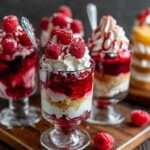 Verrines en verre composées de couches de crème vanillée, biscuits sablés émiettés, gelée de framboise et framboises fraîches entières sur le dessus.