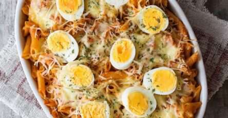 Gratin de penne aux œufs durs et fromage fondant, pâtes nappées de sauce tomate, œufs en rondelles visibles sur le dessus, surface dorée et gratinée