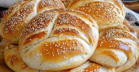 Petits pains briochés au sésame dorés au four, texture moelleuse à l’intérieur, surface brillante avec graines de sésame, disposés sur plaque de cuisson