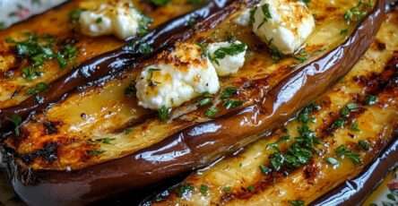 Aubergines rôties au four, chair fondante imbibée d’huile d’olive, garnies de fromage émietté et d’herbes fraîches, légèrement caramélisées