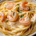 Spaghetti crémeux nappés de sauce crémeuse au parmesan avec des crevettes dorées et du persil frais, servis chauds dans une assiette.