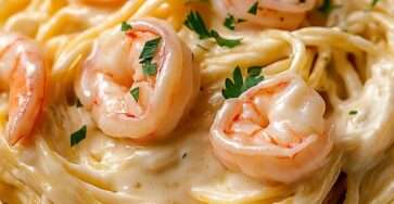 Spaghetti crémeux nappés de sauce crémeuse au parmesan avec des crevettes dorées et du persil frais, servis chauds dans une assiette.
