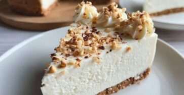 Cheesecake crémeux sans cuisson aux noisettes concassées, base biscuitée dorée et surface lisse parsemée d’éclats croquants.