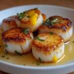 Noix de Saint-Jacques poêlées dorées, nappées de beurre citronné brillant avec persil frais, servies chaudes dans une assiette élégante.