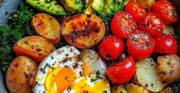 Bowl de légumes rôtis coloré, pommes de terre dorées, œufs mollets, avocat tranché et tomates cerises sur lit de verdure fraîche.