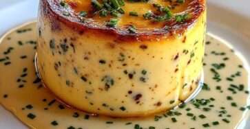 Flan de crabe démoulé, texture lisse et fondante, nappé de sauce crémeuse à la ciboulette, servi chaud dans une assiette élégante.