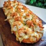 Baguette gratinée croustillante garnie de crevettes, crème onctueuse et fromage fondu doré, servie chaude avec herbes fraîches.