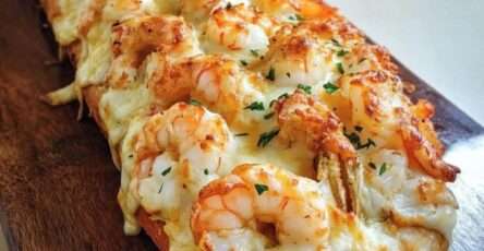Baguette gratinée croustillante garnie de crevettes, crème onctueuse et fromage fondu doré, servie chaude avec herbes fraîches.