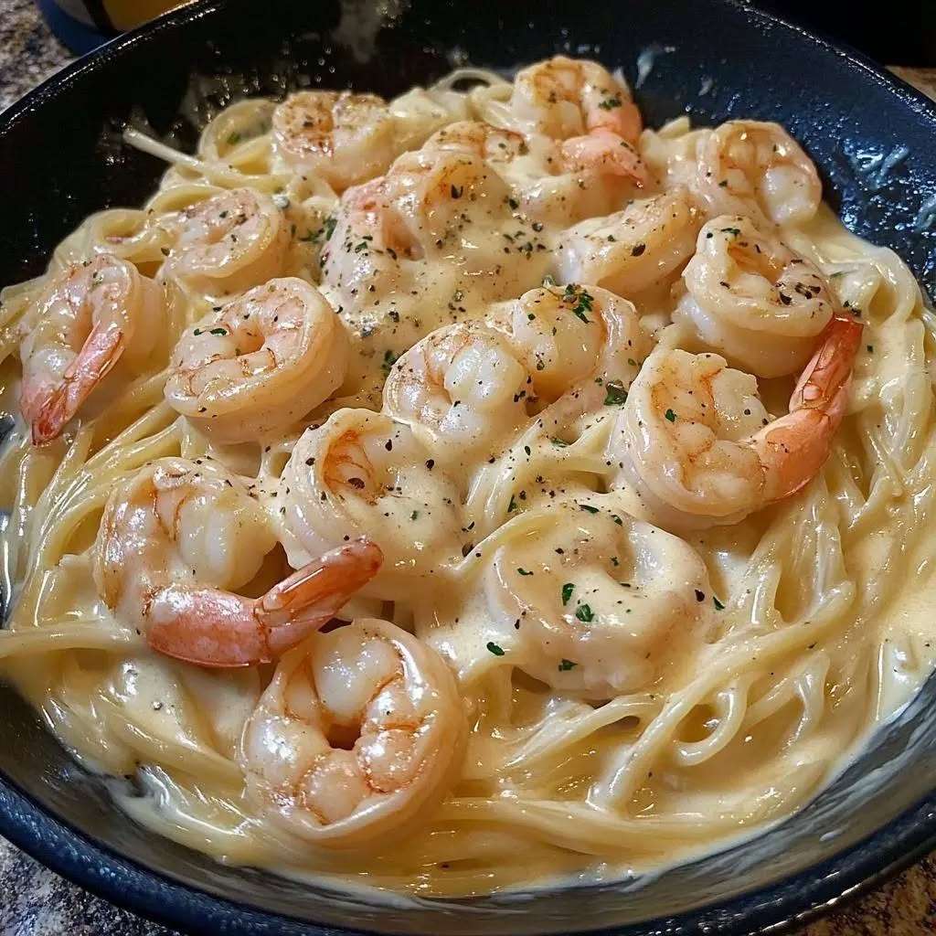 Assiette de fettuccine aux crevettes nappées de sauce Alfredo crémeuse au parmesan, parsemées de persil frais et servies chaudes.