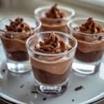 Verrines de mousse au chocolat noir onctueuse, texture aérienne et brillante, décorées de copeaux de chocolat sur le dessus dans des verres transparents.