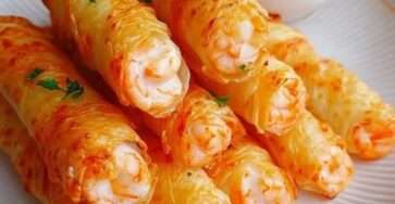 Cigares croustillants aux crevettes dorés et croustillants, servis chauds sur une assiette avec sauce au yaourt citronnée et persil frais.