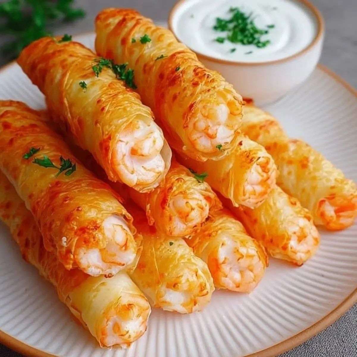 Cigares croustillants aux crevettes dorés et croustillants, servis chauds sur une assiette avec sauce au yaourt citronnée et persil frais.