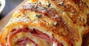 Roulé feuilleté jambon fromage tranché, pâte dorée et croustillante, fromage fondu visible à l’intérieur, servi tiède sur une planche.