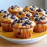 Muffins sans sucre aux myrtilles, texture moelleuse et légèrement dorée, myrtilles éclatées visibles à la surface, présentés dans des caissettes en papier sur une grille de refroidissement.