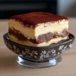 Part de tiramisu sans sucre ajouté avec couches visibles de biscuits imbibés de café et crème mascarpone onctueuse, surface généreusement saupoudrée de cacao amer non sucré.