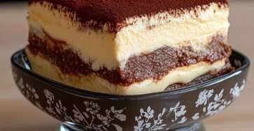 Part de tiramisu sans sucre ajouté avec couches visibles de biscuits imbibés de café et crème mascarpone onctueuse, surface généreusement saupoudrée de cacao amer non sucré.