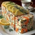 Tranches de terrine crémeuse aux crevettes roses et herbes fraîches, texture lisse et fondante, décorée de rondelles de citron et pluches d’aneth, servie sur un plat blanc.