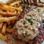 Steak grillé nappé de sauce crémeuse aux champignons, accompagné de frites maison dorées et croustillantes, servi dans une assiette rustique