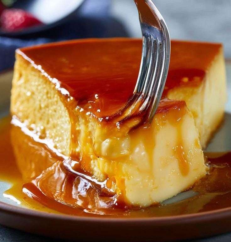 Flan vénézuélien ultra crémeux démoulé sur un plat, nappé de caramel ambré coulant, surface lisse et brillante, part découpée montrant une texture fondante.