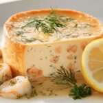 Flan de poisson au saumon et citron démoulé sur assiette, texture fondante, parsemé d’aneth frais, accompagné de rondelles de citron.