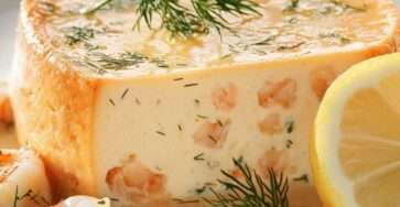 Flan de poisson au saumon et citron démoulé sur assiette, texture fondante, parsemé d’aneth frais, accompagné de rondelles de citron.