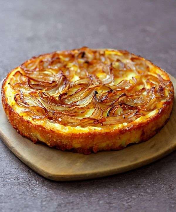 Gâteau salé moelleux aux oignons dorés et fromage fondu, coupé en parts, mie fondante, servi tiède sur une planche avec salade.