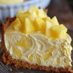 Cheesecake sans cuisson à l’ananas sur base biscuitée, crème lisse et épaisse, morceaux d’ananas juteux sur le dessus, part découpée montrant les couches.