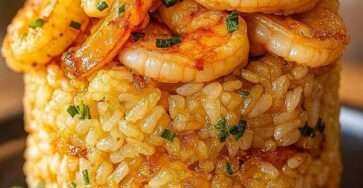 Tour de riz crémeux aux crevettes dorées au beurre à l’ail, garnie de ciboulette fraîche et parmesan, dressée en forme de dôme dans une assiette.