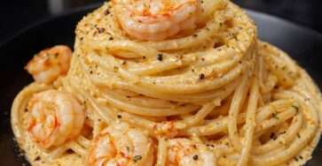 Volcan de pâtes spaghetti crémeux au parmesan garni de crevettes dorées et persil frais dans une assiette.