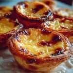 Pastéis de nata portugais dorés avec pâte feuilletée croustillante et crème vanillée légèrement caramélisée, saupoudrés de sucre glace et cannelle.