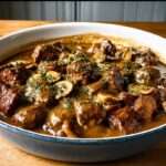 Joue de bœuf mijotée aux champignons servie dans une cocotte, avec morceaux de viande fondants, carottes, sauce brune brillante et persil frais.
