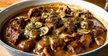 Joue de bœuf mijotée aux champignons servie dans une cocotte, avec morceaux de viande fondants, carottes, sauce brune brillante et persil frais.