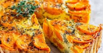 Tarte fondante aux carottes cuite au four, garnie de rondelles de carottes tendres, de fromage gratiné et d’herbes aromatiques, servie dans un moule doré.