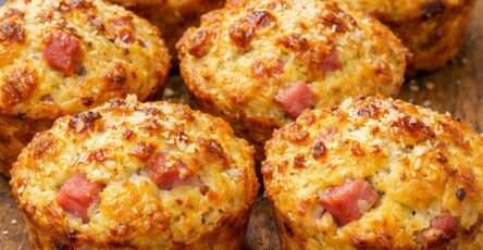 Muffins salés dorés au jambon et fromage, moelleux à l’intérieur avec une croûte gratinée au parmesan, servis tièdes sur une table.