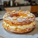 Couronne feuilletée dorée garnie de crème vanillée légère, décorée d’amandes effilées et saupoudrée de sucre glace.