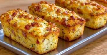 Financiers salés au jambon et fromage dorés, moelleux à l’intérieur, servis chauds avec herbes fraîches sur une table d’apéritif.