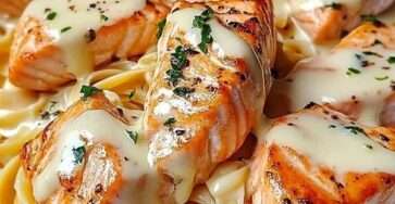 Assiette de pâtes crémeuses au saumon grillé avec sauce au fromage fondue, morceaux de saumon dorés et persil frais en finition.