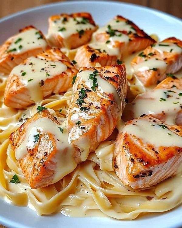 Assiette de pâtes crémeuses au saumon grillé avec sauce au fromage fondue, morceaux de saumon dorés et persil frais en finition.